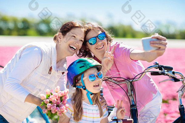 荷兰一家人在荷兰郁金香花圃里骑自行车。母亲和孩子们在花开的自行车上用手机<strong>拍照</strong>自拍