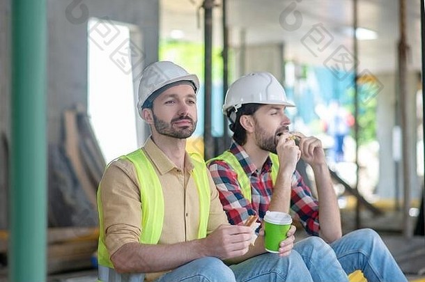 建筑工人黄色的背心头盔坐着咖啡三明治