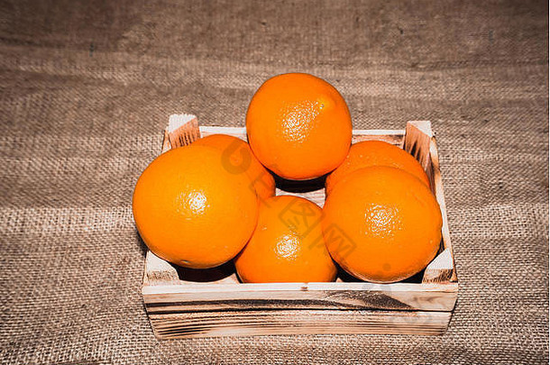 新鲜成熟的橙色水果放在旧的烧焦木箱或麻布背景的盒子里。添加复古和复古效果。