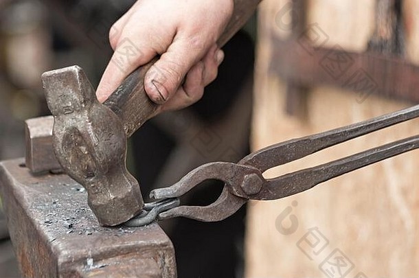 铁匠用锤子和钳子在铁砧上锻造铁环。