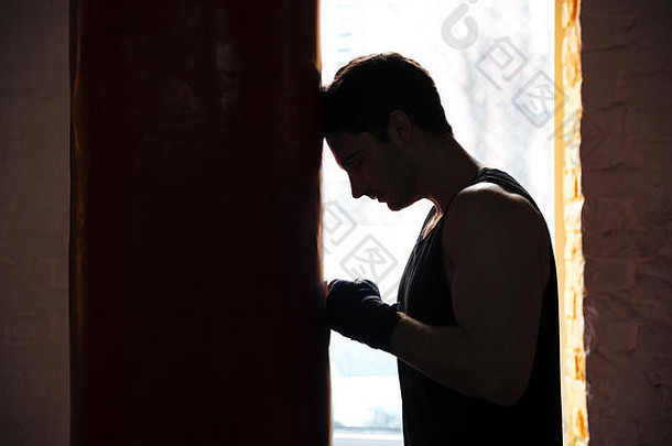 疲惫的运动员拳击手在训练时倚着红色的拳击袋