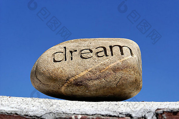 梦想被放在架子上，一块刻有“梦想”字样的石头坐落在一堵砖墙顶上，映衬着深蓝色的天空