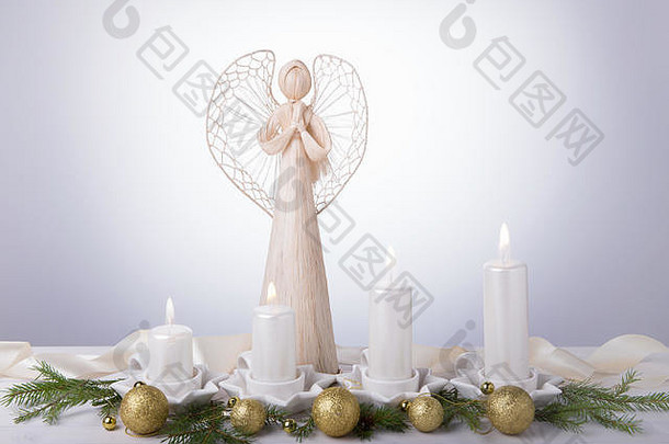一位白色的天使和四支白色的降临蜡烛，圣诞树枝上装饰着金球。即将到来的降临节和圣诞节的背景。