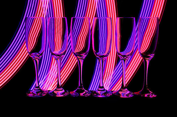 一排六个空香槟酒杯/长笛，在黑色背景上相互隔离，后面有彩色霓虹灯<strong>条</strong>纹的光画
