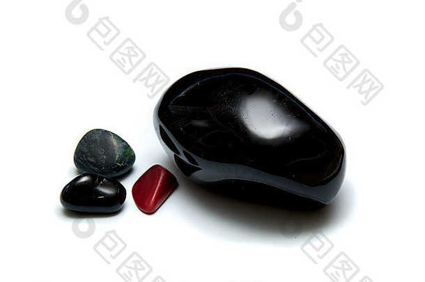 四块光滑的黑色岩石的集合，用于在白色表面按摩。一块大石头和三块小石头。