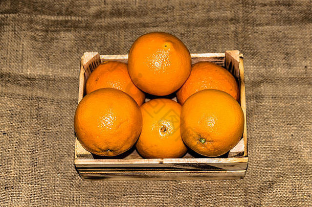 新鲜成熟的橙色水果放在旧的烧焦木箱或麻布背景的盒子里。添加复古和复古效果。
