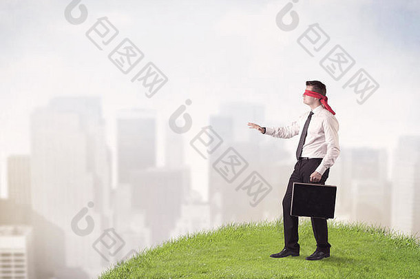 年轻的蒙着眼睛的商人踩在一片草地上，背景是一座城市