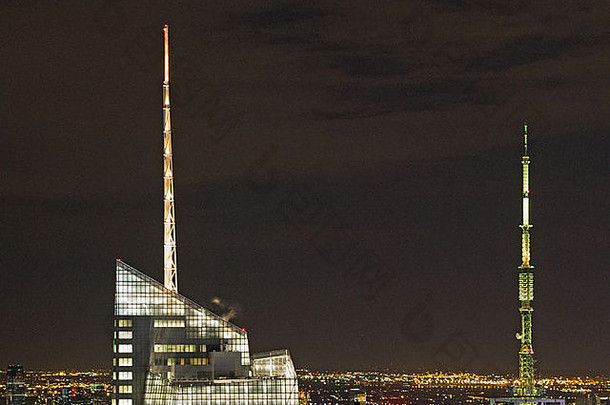 曼哈顿天际线的夜间拍摄，显示两个桅杆，一座建筑物上升起一缕小蒸汽，导航灯点亮