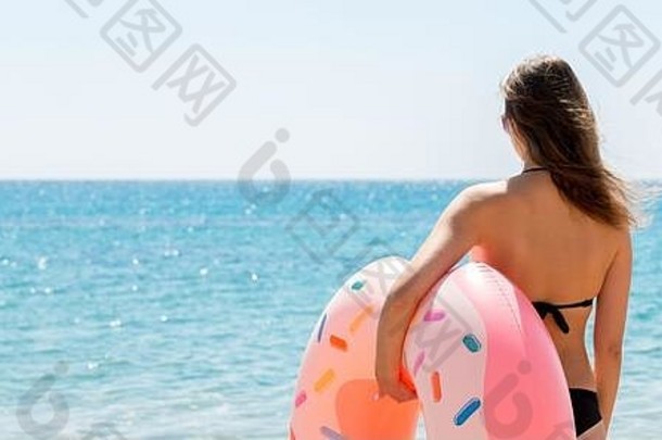 回来视图年轻的女人持有甜甜圈橡胶环走海热夏天