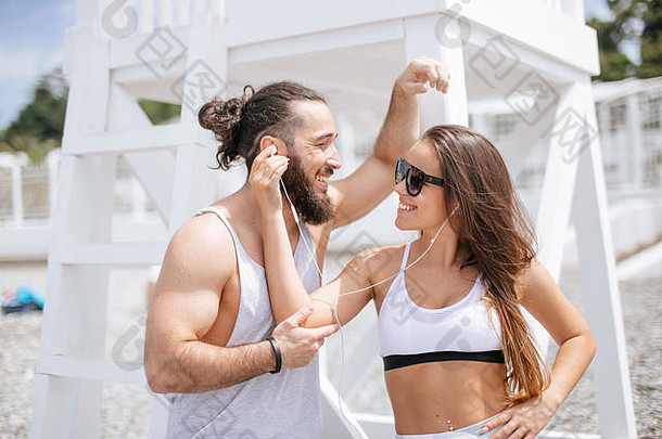 一对年轻夫妇在海滩上用一个耳机听音乐