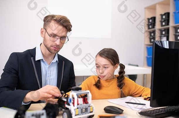 <strong>男老师</strong>和女孩坐在桌子旁，看着可建造的汽车