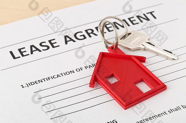 带有红色房屋钥匙链挂件的房屋门钥匙和木质书桌上的租赁协议表-房屋或公寓租赁概念