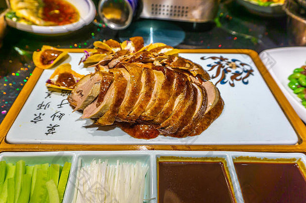 中国北京烤鸭片，盛在盘子里，配上蔬菜和酱油