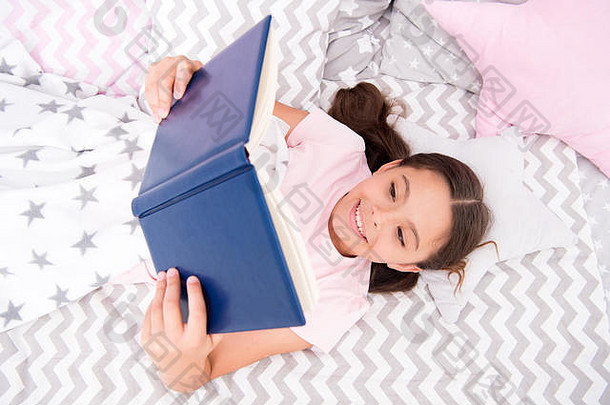 女孩躺在床上看书。鼓励孩子养成有用的<strong>习惯</strong>。孩子准备睡觉。在舒适的卧室里度过愉快的时光。女孩孩子长头发可爱的睡衣放松和看书。满意的幸福结局。