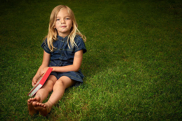 可爱的金发小女孩在外面草地上看书