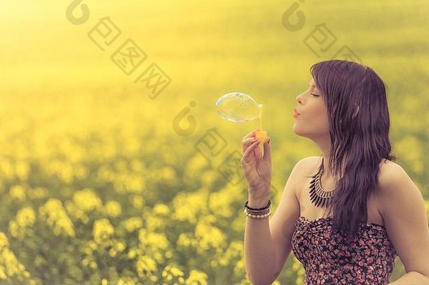 美丽的女人在黄色的夏日草地上吹肥皂泡。这个女孩在大自然中很快乐，<strong>正</strong>在享受她的<strong>青春</strong>。