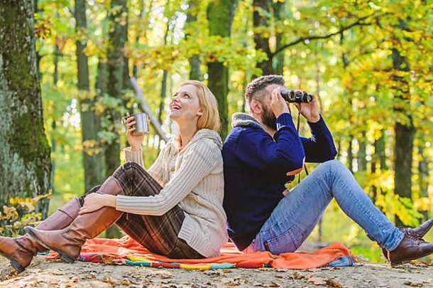 停车日期。一起在公园里放松。一对幸福的情侣一起在公园里放松。情侣恋爱游客放松<strong>野餐</strong>毯。男人拿着双筒望远镜，女人拿着金属杯子，享受着自然公园。