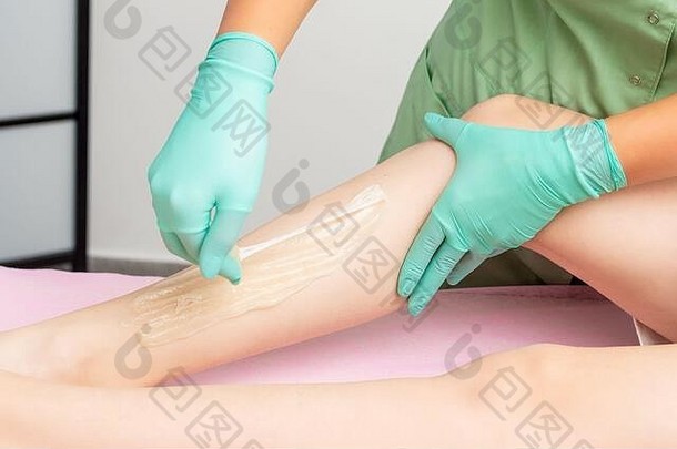脱毛过程中，美容师用手在妇女腿上打蜡。