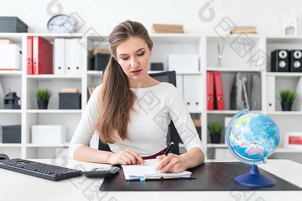 一个年轻女孩坐在桌子旁，在一张纸上写字。