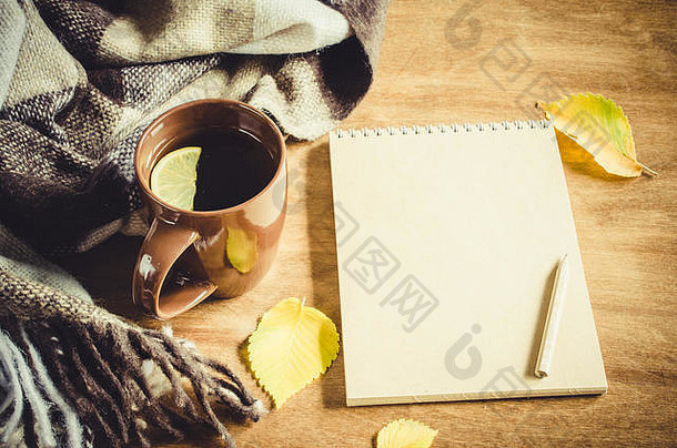 一杯柠檬热茶，一本素描用的空笔记本，一张朴素的桌子上的格子布，黄色的叶子。温馨的秋意，温暖的秋天。