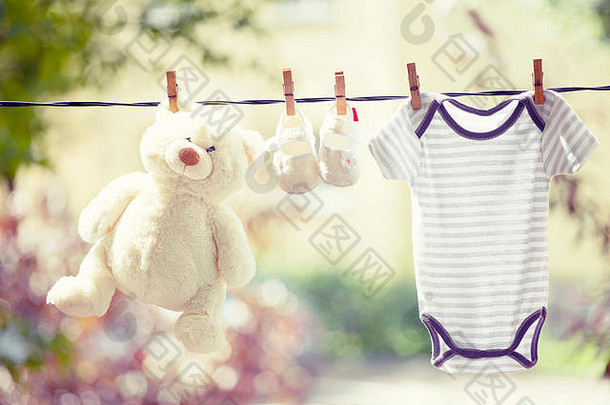婴儿服装、靴子和挂在晾衣绳上的泰迪熊-家庭概念、新生儿概念
