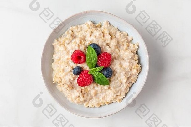 碗中的燕麦粥，白色背景上有新鲜浆果和薄荷，是健康饮食早餐。俯视图