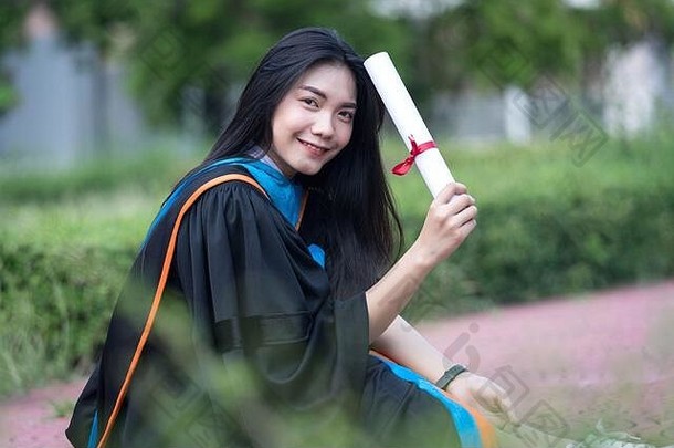 在大学校园里，年轻的亚洲女大学毕业生穿着毕业礼服，戴着毕业帽，喜气洋洋，喜气洋洋。