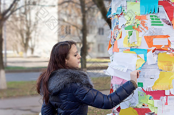 年轻的女人阅读请注意公共警告牌在户外覆盖色彩鲜艳的笔记广告