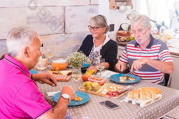 一群老<strong>年</strong>人在家一起吃午饭。她微笑着，其他人认真地吃着。桌上的意大利腊肠面包和蔬菜
