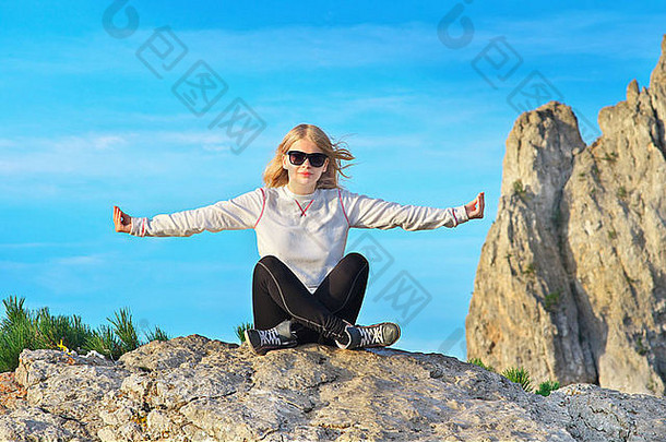 女旅行者放松瑜伽冥想坐在石头上放松，背景是落基山和蓝天