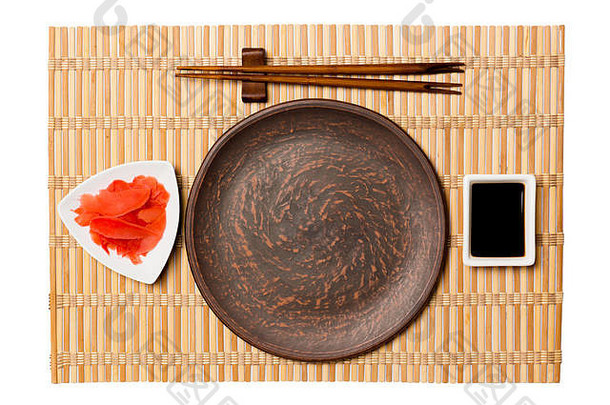 空的圆形棕色盘子，用筷子盛寿司和酱油，黄色竹垫背景上放生姜。带有供您设计的空间的俯视图。
