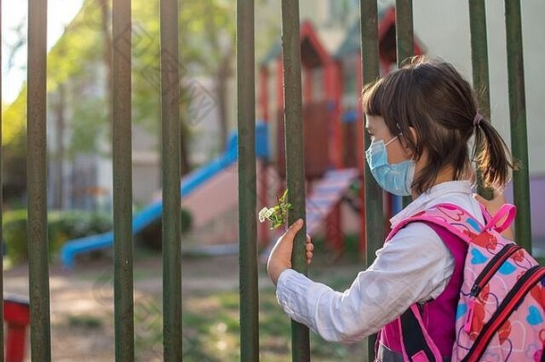 流感爆发后，坐在学校围栏旁等待重返校园的小女生