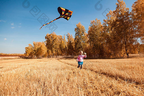 秋季生活方式和家庭户外休闲的概念。在一个温暖的秋日阳光明媚的日子里，一个金发开朗的女孩喜欢大自然，玩风筝