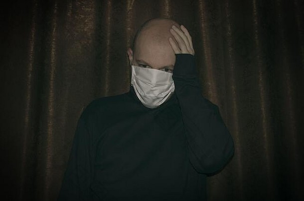 秃头男人戴着口罩隔离以<strong>保护自己</strong>免受冠状病毒的侵害。。沮丧的男人双手捂着头