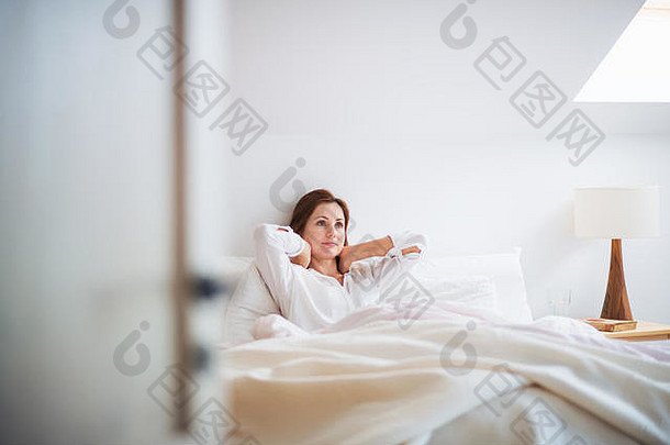 年轻的女人坐着床上在室内早....卧室休息