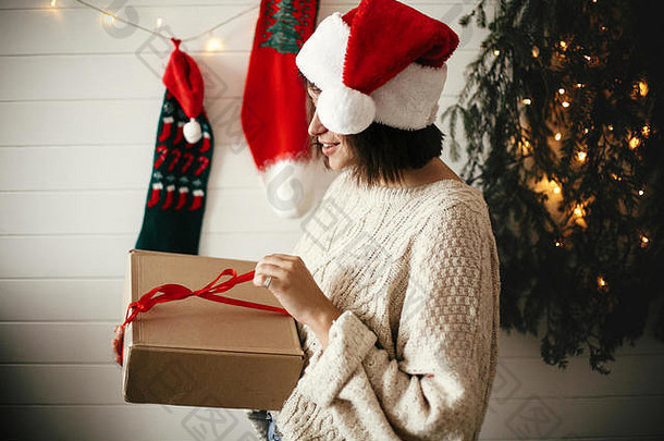 时尚的快乐女孩节日毛衣圣诞老人他开放礼物盒子背景现代圣诞节树灯长袜时尚的房间