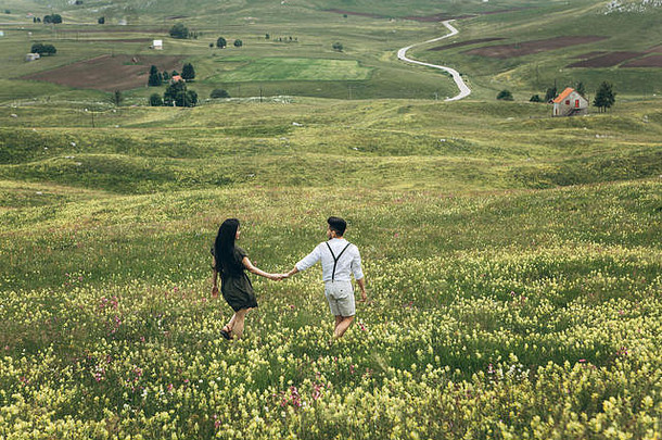 一对年轻夫妇在草地上共度时光。暑假或无忧无虑的时间。他们跑步，玩得很开心。