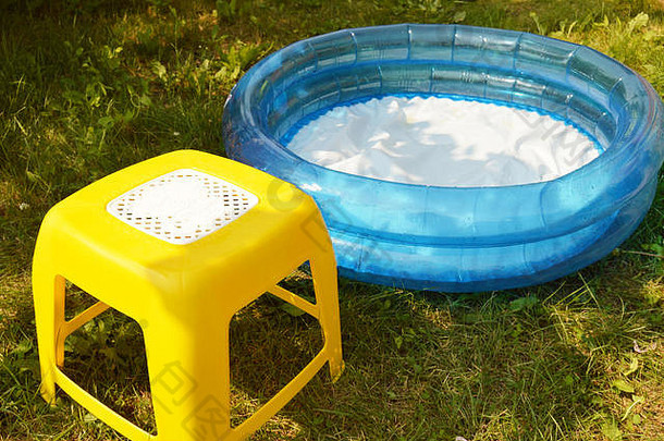 在一个阳光明媚的<strong>夏日</strong>，孩子们的充气<strong>游泳</strong>池和一把小椅子站在绿草上