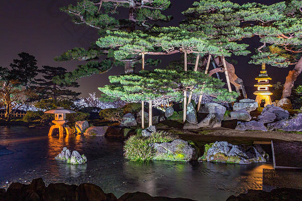 在日本石川县金泽县健鲁川花园，松树、池塘和Kotoji toro灯笼的长曝光（无闪光）夜景。肯罗库恩