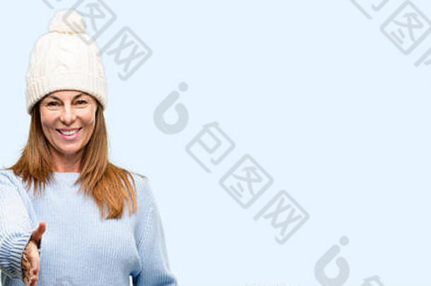 戴羊毛冬帽的中年妇女以握<strong>手</strong>的<strong>姿势</strong>握<strong>手</strong>表示欢迎，表达信任和成功的概念，问候与世隔绝的蓝色背景