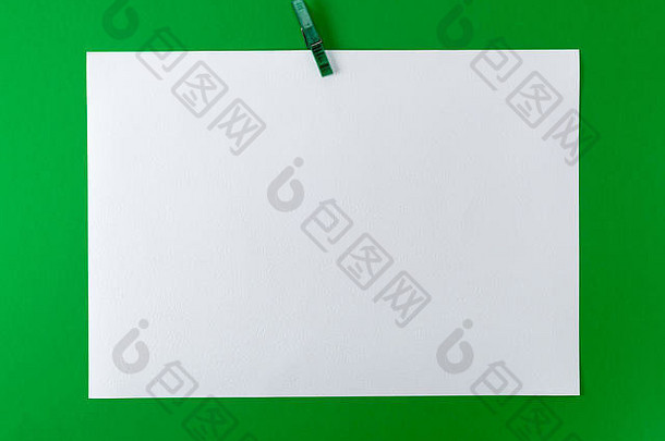 绿色塑料衣夹上的白色空白图纸，绿色背景