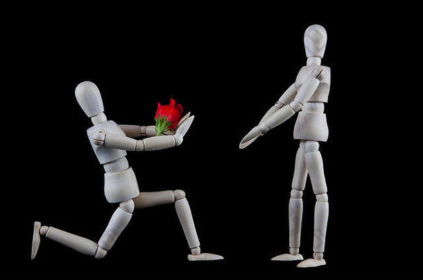 婚礼、订婚建议或情人节概念。跪着的木制雕像在黑色背景上向站立的雕像献花，并留有空间