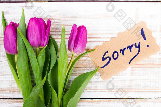 “对不起”和木质背景上的郁金香花束
