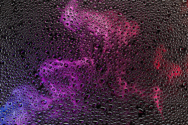 在黑色背景上，一滴水在紫色、粉色和蓝色烟雾的衬托下特写，在渐变背景上凝结