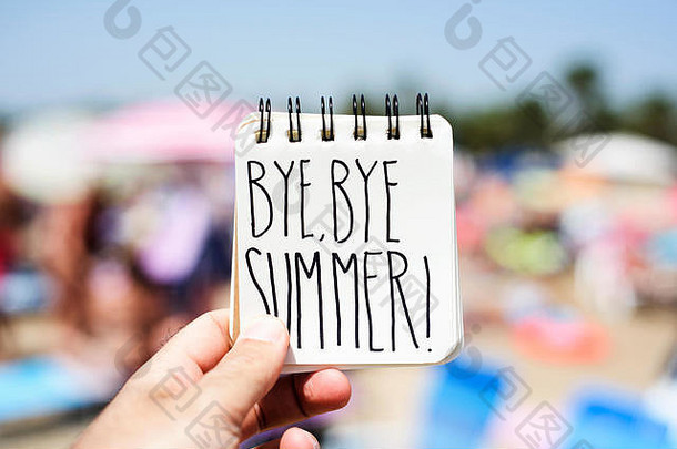 海滩上一个年轻人的特写镜头显示了一个螺旋形记事本，上面手写着“再见，夏天”