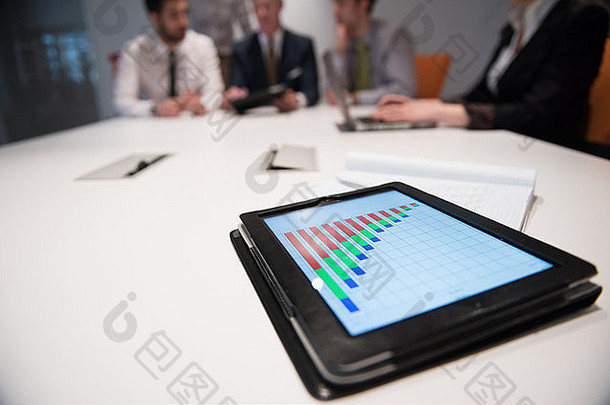 平板触摸屏电脑特写，重点关注业务分析和进度图文档。商务人士小组会议