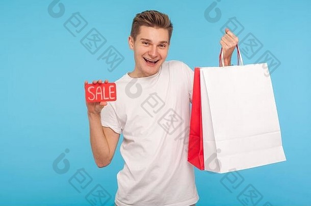 兴奋的快乐男人拿着销售标语和购物袋，对着镜头热情地微笑，看起来对优<strong>惠</strong>很满意，黑色星期五