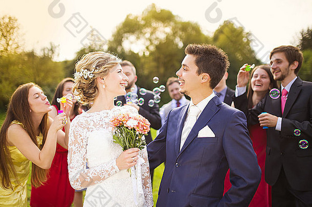 年轻的新婚夫妇在外面的婚礼招待会上一起享受<strong>浪漫</strong>时刻，婚礼宾客在后台吹泡泡