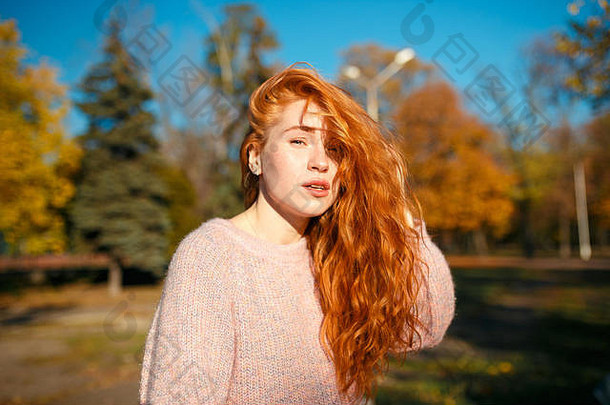 一个迷人的红发女孩的肖像，一张可爱的脸。穿着毛衣和<strong>珊瑚色</strong>裙子的女孩在秋天公园摆姿势。这个女孩有一个很棒的孩子