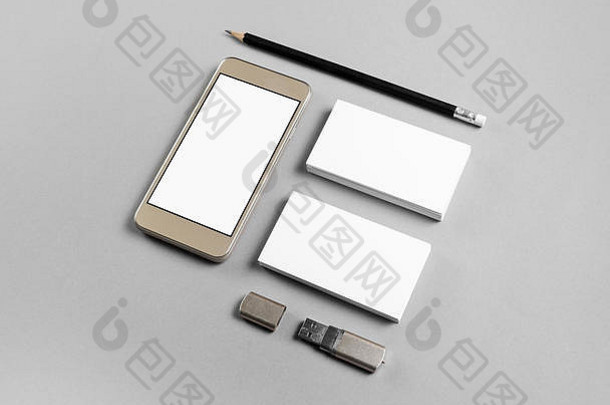 空白名片、铅笔、usb闪存驱动器和智能手机，灰色纸张背景上有空白屏幕。智能手机和文具